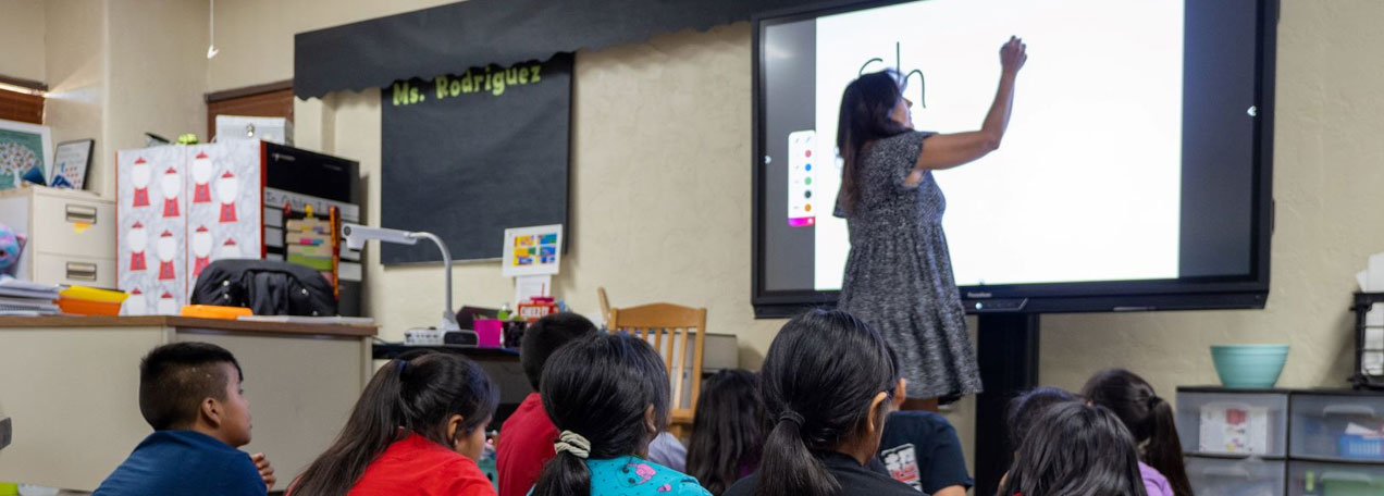 The teacher is writing on a digital board while the students pay attention to the lesson.