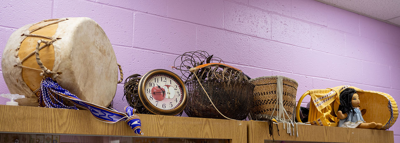 Drums, clock, basket sitting on a bookshelf. 