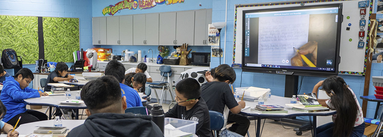 Classroom of students watching a digital board. 