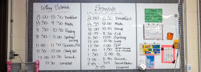Daily class schedule written on a whiteboard. 